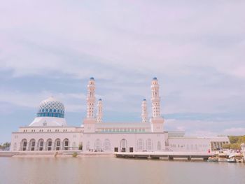 Sabah state mosque by lake against cloudy sky