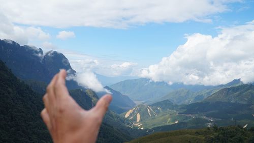 Optical illusion of hand holding cloud against mountains