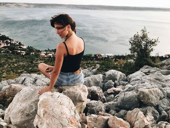 Rear view of young woman sitting on mountain against sea