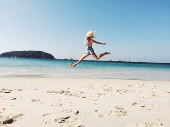 Full length of woman jumping at beach against clear sky