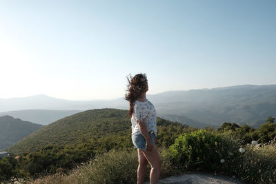 Rear view of woman standing on mountain against clear sky