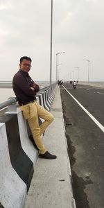 Full length portrait of young man sitting against sky