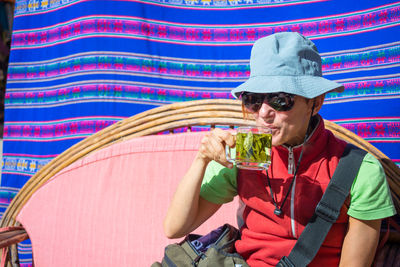 Mature woman wearing sunglasses and hat having tea while sitting on sofa at yard