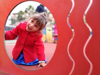 Cheerful girl seen through hole on outdoor play equipment