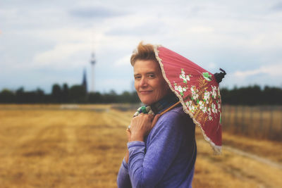 Portrait of smiling woman holding umbrella while standing on field against sky