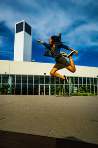 Young woman jumping by built structure against sky