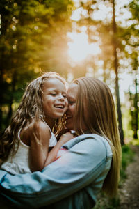 Happy mom and daughter laughing and snuggling in backlit forest