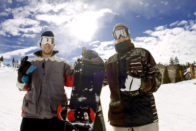 Portrait of happy snowboarders standing against cloudy sky