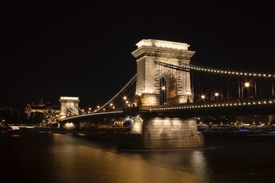 Illuminated bridge over river in city at night