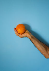 Orange in hand on blue wall