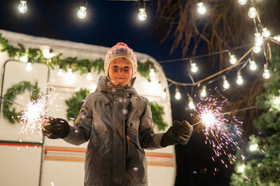 Portrait of woman standing against illuminated christmas tree