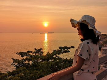 Woman looking at sea against sky during sunset