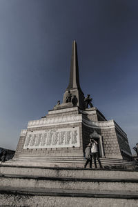 Low angle view of friends standing by victory monument against clear sky