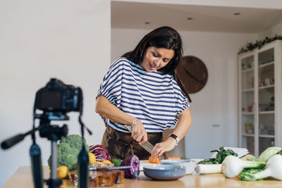 Woman cutting carrot filming through camera at home