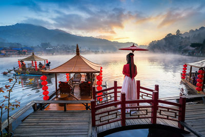 Rear view of woman standing by lake against sky