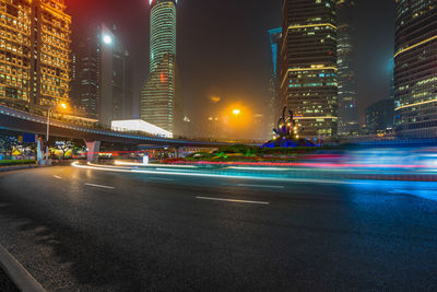 Light trails on road by illuminated buildings in city at night