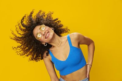 Portrait of young woman standing against yellow background