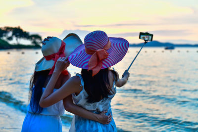 Rear view of women taking selfie on mobile phone against sea and sky