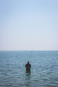 Rear view of man fishing in sea against clear sky