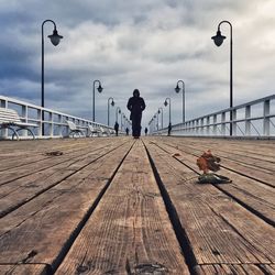 People walking on pier against cloudy sky
