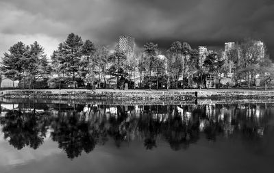 Reflection of trees in lake against sky in city
