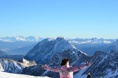 Man with arms outstretched against snowcapped mountains