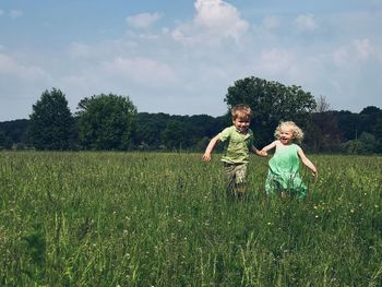 Cheerful siblings holding hands while running on grassy field