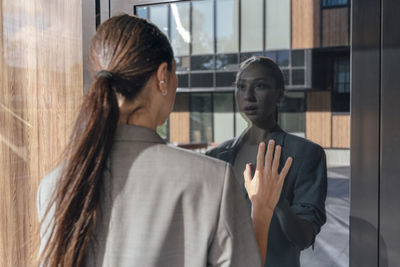 Businesswoman looking at reflection on glass door