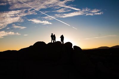 Silhouette people standing on rocks against sky during sunset