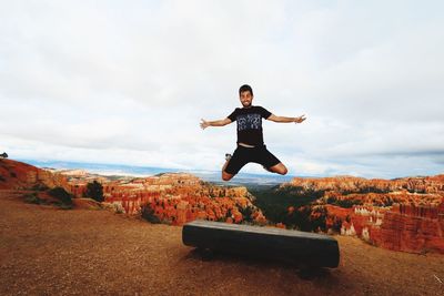 Portrait of young man jumping on mountain against cloudy sky