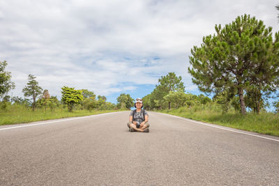 Man sitting on road against sky