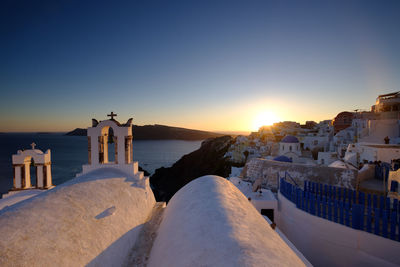 Buildings by sea against clear sky during sunset