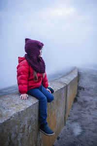 Rear view of boy sitting on rock by sea against sky