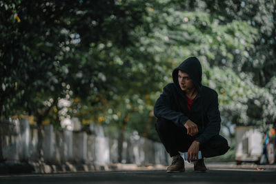 Thoughtful young man with phone crouching on road