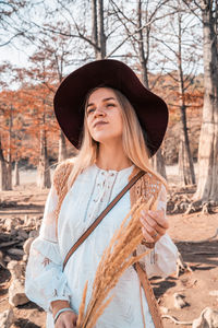 Young woman wearing hat standing against trees