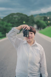 Young woman photographing with camera while standing on road