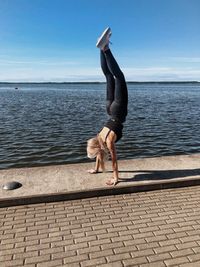 Full length of woman practicing handstand on promenade against sky