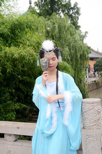 Woman wearing traditional clothing covering face by mirror outdoors