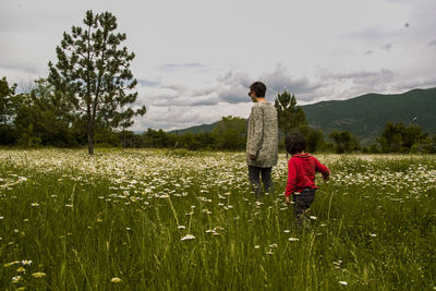 Woman with daughter walking in chamomile field against sky
