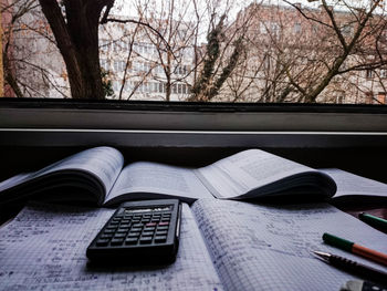 Close-up of calculator and books by window sill