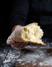 Close-up of person holding bread on table against black background