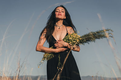 Young woman standing by plant against sky