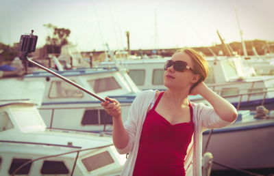 Young woman holding monopod while taking selfie through smart phone at harbor