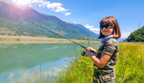 Young man wearing sunglasses standing by lake against sky