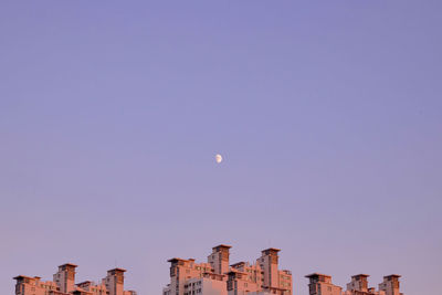 Low angle view of buildings against clear sky and moon