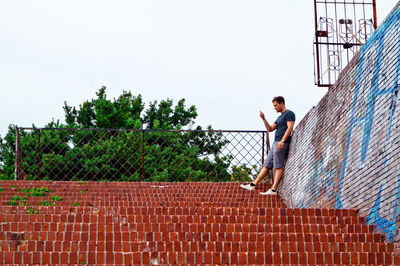 Man standing on steps by trees against sky