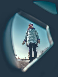 Low angle view of woman standing on road seen through wheel