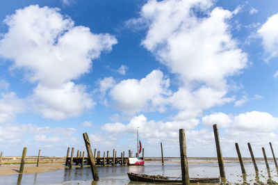 Wooden posts at beach against cloudy sky