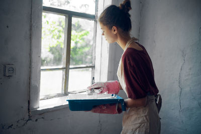 Side view of a young woman standing against window