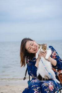 Woman relax sit on beach chair and hug her cat on sand beach